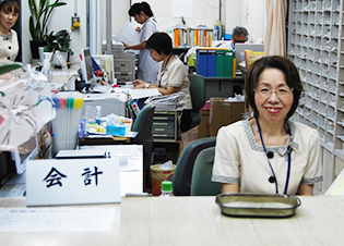 介護施設の事務室で働くスタッフ。会計業務を担当する職員が笑顔で対応している様子。