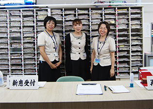介護施設のスタッフ3名が受付エリアで勤務している様子。背後に書類整理棚がある。